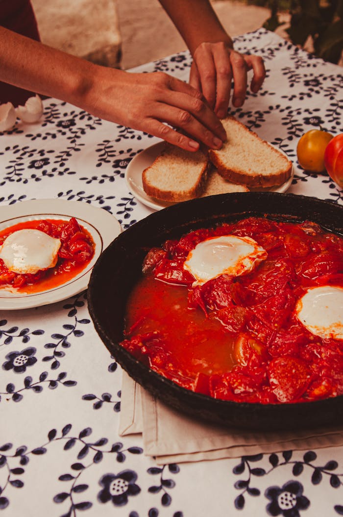 A vibrant dish of shakshuka with eggs in tomato sauce, ready to be served with fresh bread slices.