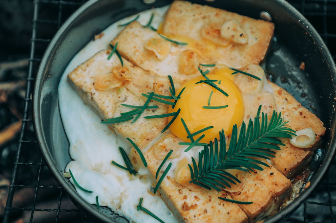 From above appetizing grilled toasts under egg with rosemary cooked on frying pan on barbecue grid