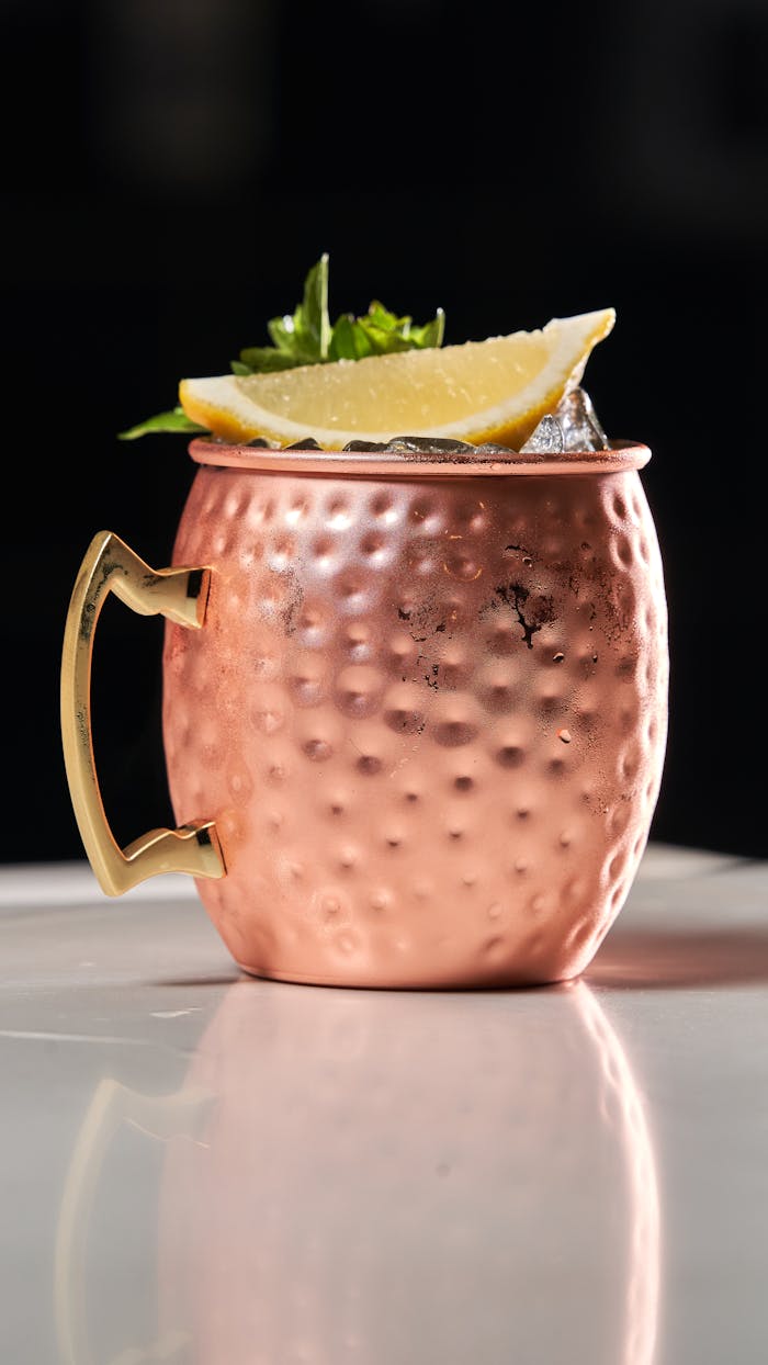 Copper mug with a Moscow Mule and lemon garnish on a reflective surface.
